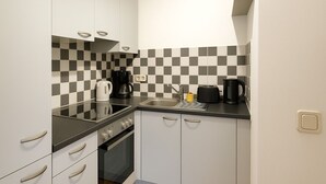 A compact kitchen with white cabinets, a black countertop, and a checkered backsplash. - StayINN - Leipzig, BSS25a (Leipzig)