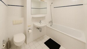 A bathroom with a toilet, sink, mirror, and bathtub. - StayINN - Leipzig, BSS25a (Leipzig)
