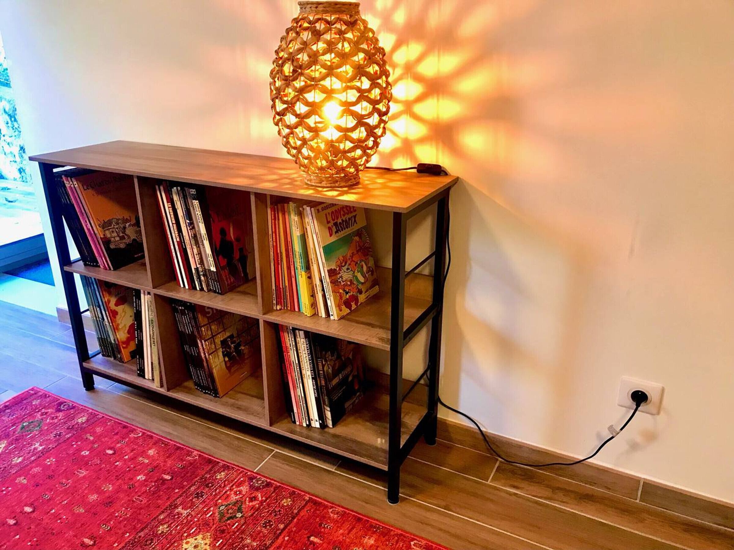 Ein Bücherregal aus Holz mit Büchern, einer Zierlampe und einem roten Teppich.