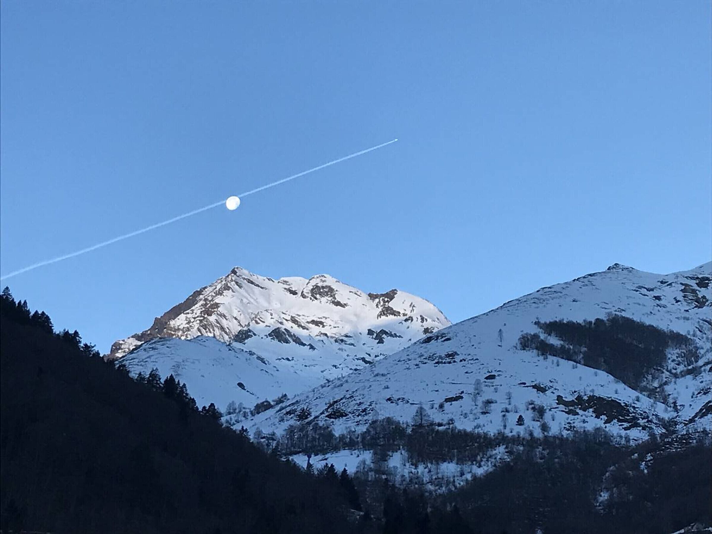 Montanha coberta de neve com céu claro e rastro de condensação visível.