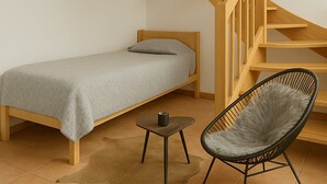 Une chambre avec un lit simple, une chaise, une petite table et un escalier en colimaçon en bois.