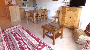 Una sala de estar acogedora con un sofá, una mesa de comedor de madera, sillas, una mesa de centro y una televisión.