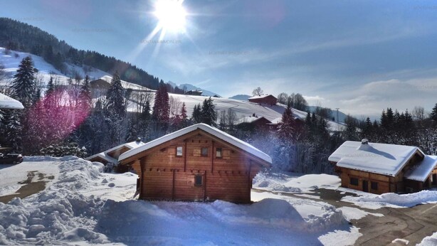 Un pintoresco pueblo de montaña nevado con cabañas de madera, cielo despejado y un sol brillante.