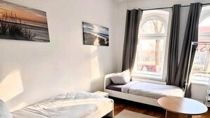 A modern room with a bed, a small table, a bench, and a window with curtains. - Apartment Halle city center - 2 rooms (Halle (Saale))