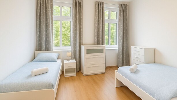 A bedroom with two single beds, a bedside table with a lamp, a dresser, and a window with curtains. - Apartment Halle city center - 2 rooms (Halle (Saale))