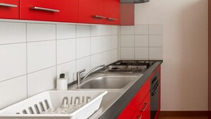 A kitchen with red cabinets, a black countertop, a stainless steel sink, and a built-in oven. - Apartment Halle city center - 2 rooms (Halle (Saale))