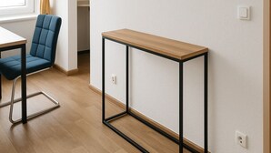 A modern room with a flat-screen TV mounted on the wall, a wooden table with black metal legs, a blue upholstered chair, and a window with yellow curtains. - Apartment Halle city center - 3 rooms (Halle (Saale))