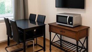 Un coin repas avec une table et des chaises, un four à micro-ondes posé sur une petite table en bois, et un téléviseur fixé au mur.