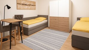 Une chambre à coucher de taille modeste, comprenant un lit, un bureau, une chaise, une armoire et un tableau accroché au mur.