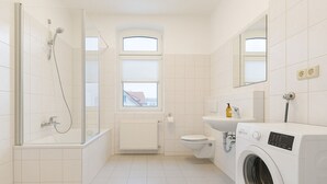 Une salle de bain moderne équipée d’une douche, de toilettes, d’un lavabo et d’un lave-linge.