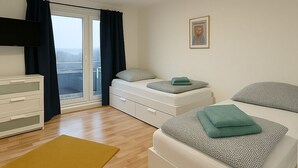 A modern bedroom with a bed, a sofa, a TV, a window with curtains, and a small artwork on the wall.