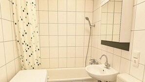 A small bathroom with a toilet, sink, shower, and a washing machine.