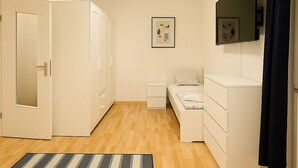 A room with a bed, a bedside table, a wardrobe, a mirror, and a striped rug.