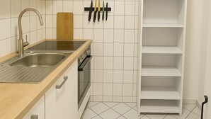 A kitchen with white cabinets, a stainless steel sink, a wooden countertop, a hanging knife rack, and a white shelving unit.