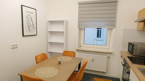 Et moderne køkken med mikrobølgeovn, ovn og vask. Der er et spiseområde med bord og stole, samt et vindue med persienner.