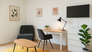 Et moderne værelse med et skrivebord, to stole, et fjernsyn og billeder hængende på væggen.