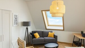 A modern loft bedroom with a sloped ceiling, a grey sofa with yellow cushions, a round black coffee table, wooden chairs, a standing lamp, and a framed picture on the wall. - House Delitzsch Holzstraße - 8 beds, parking lot (Delitzsch)