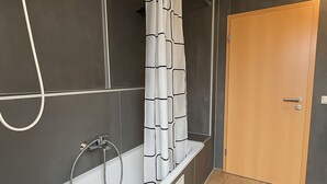 A modern bathroom with a white bathtub, shower, and a wooden door. - House Delitzsch Holzstraße - 8 beds, parking lot (Delitzsch)