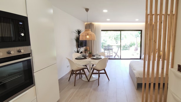 Une cuisine moderne dotée d’appareils électroménagers intégrés, un coin repas avec une table ronde et des chaises, et une vue sur l’extérieur grâce à de grandes fenêtres.