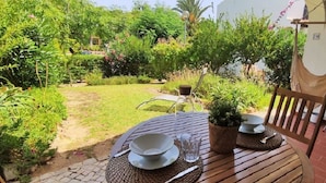Un espace extérieur aménagé pour les repas, avec une table dressée pour deux personnes, entouré d’une végétation luxuriante et agrémenté d’un barbecue.