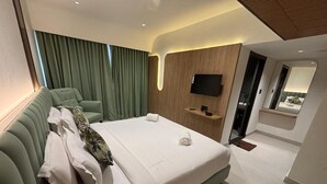 A modern hotel room with a green sofa, a large bed, a flat-screen TV, and a wooden accent wall. - Yuvraj Landmark (Mysore)