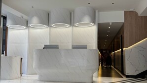 A modern reception area with a marble reception desk, cylindrical wall sconces, and a geometric ceiling light fixture. - Yuvraj Landmark (Mysore)