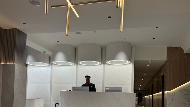 A modern reception area with a marble reception desk, a check-in counter, and a staircase leading to upper floors. - Yuvraj Landmark (Mysore)