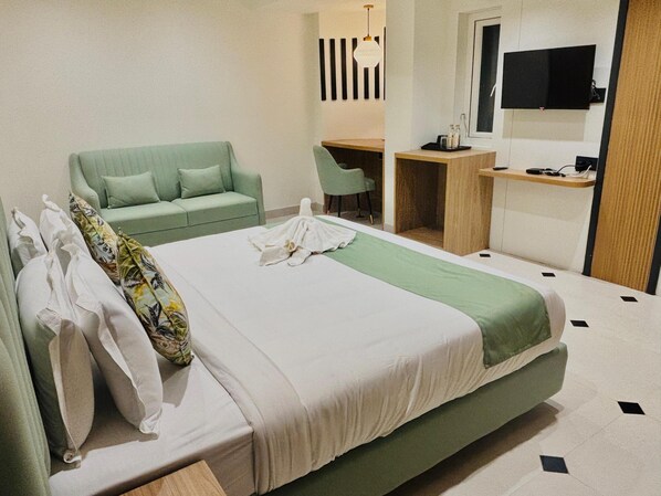 Une chambre d’hôtel avec un lit, un canapé vert, un bureau et une télévision.