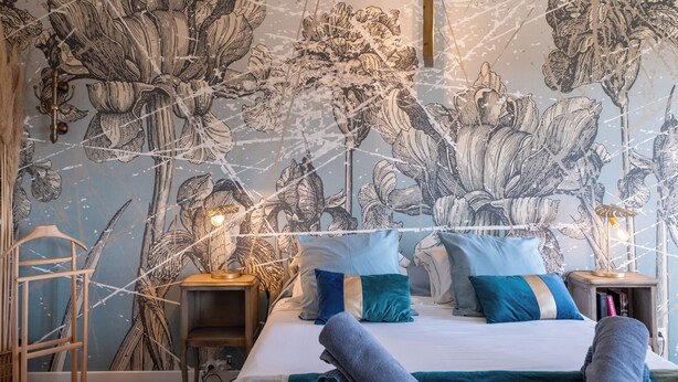 Ein Schlafzimmer mit einem großen Bett, zwei Nachttischen, einem Holzstuhl und einer Wand mit einem floralen Muster.