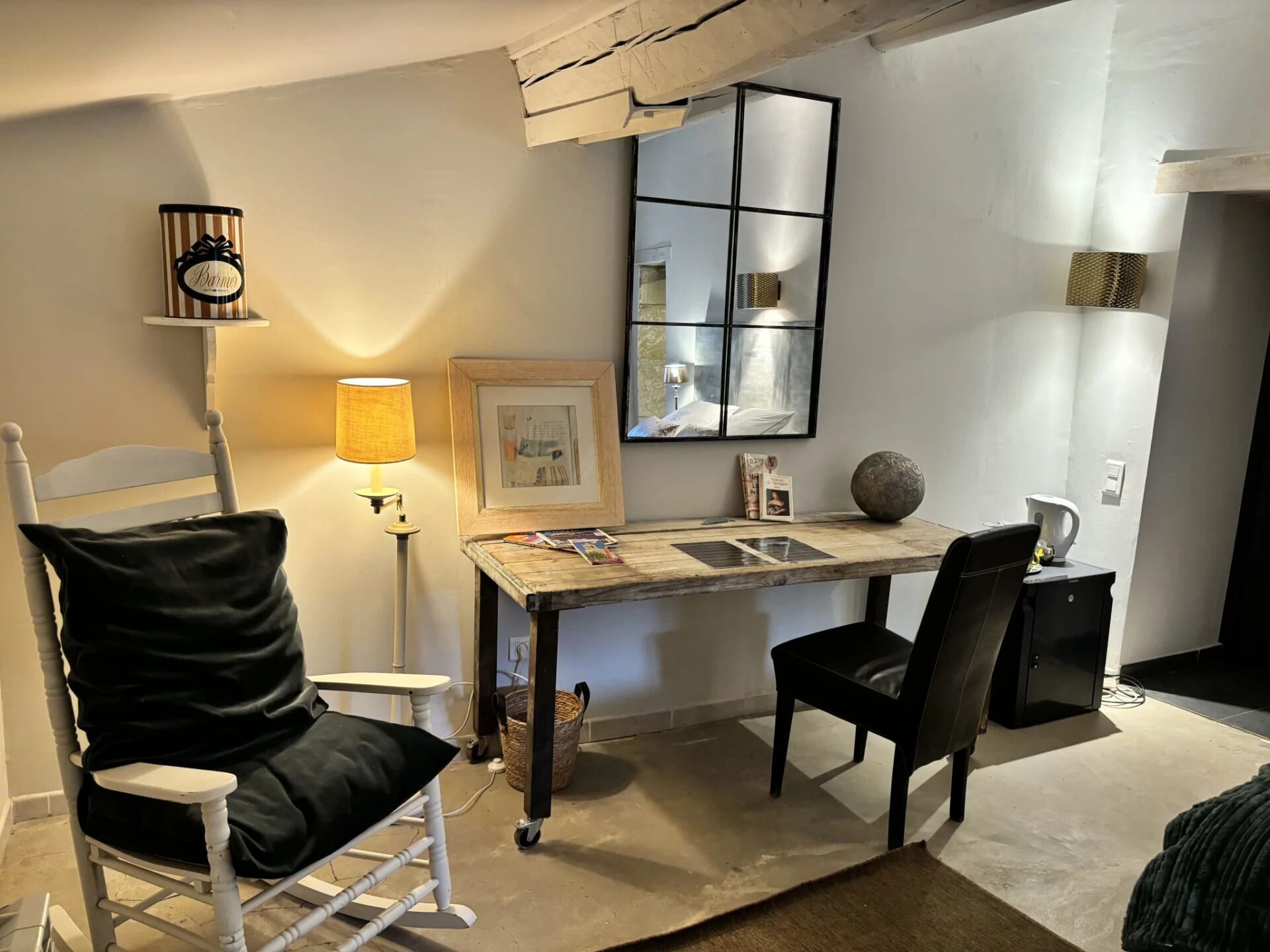A small, modern room with a desk, two chairs, a lamp, a framed picture, and a decorative mirror.