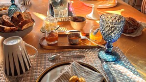 Ein Esstisch ist reichhaltig mit Speisen gedeckt, darunter Brot, Gebäck und eine dekorative Vase mit Blumen.