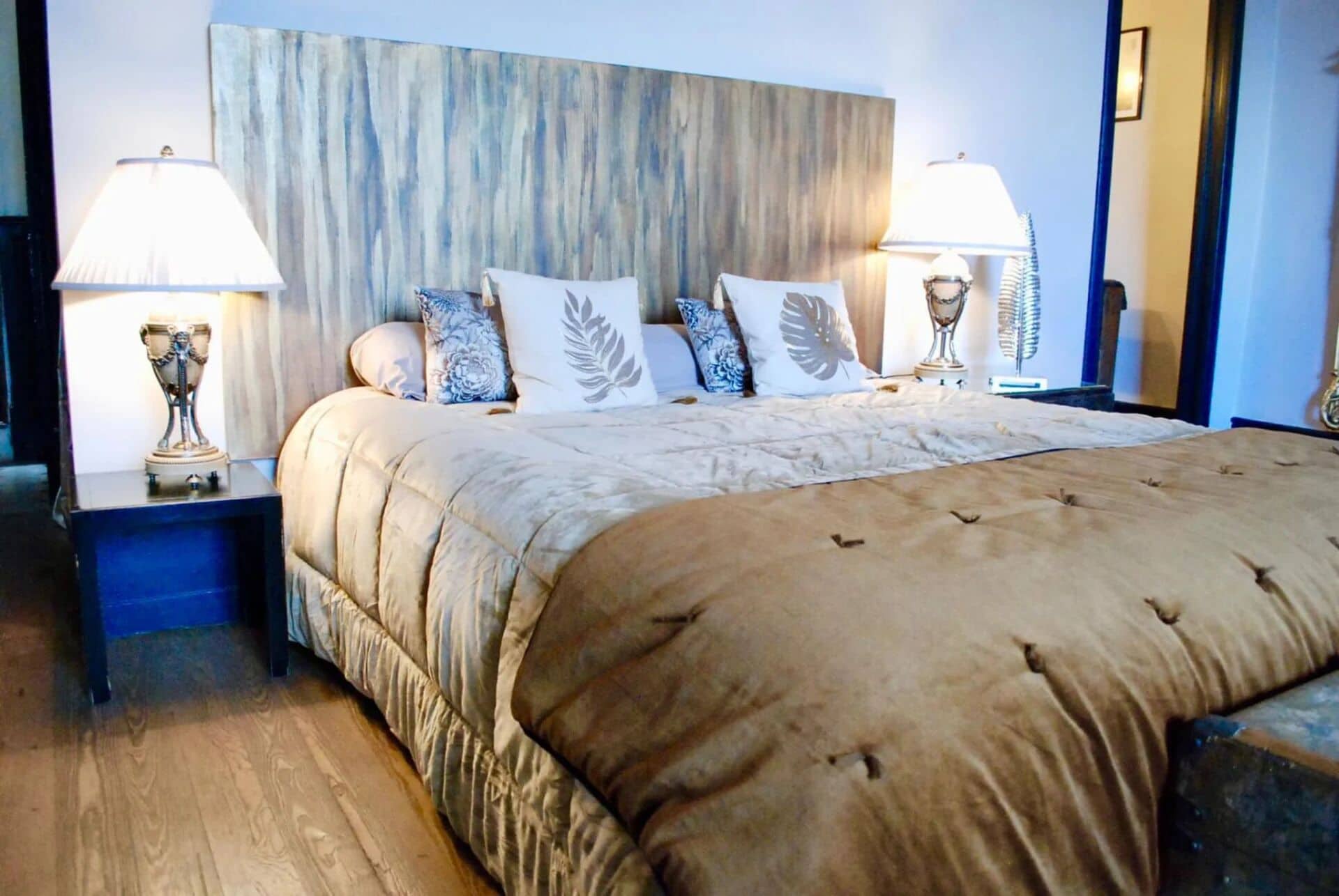A neatly made bed with a beige duvet and decorative pillows, flanked by two bedside tables with lamps and a decorative vase.