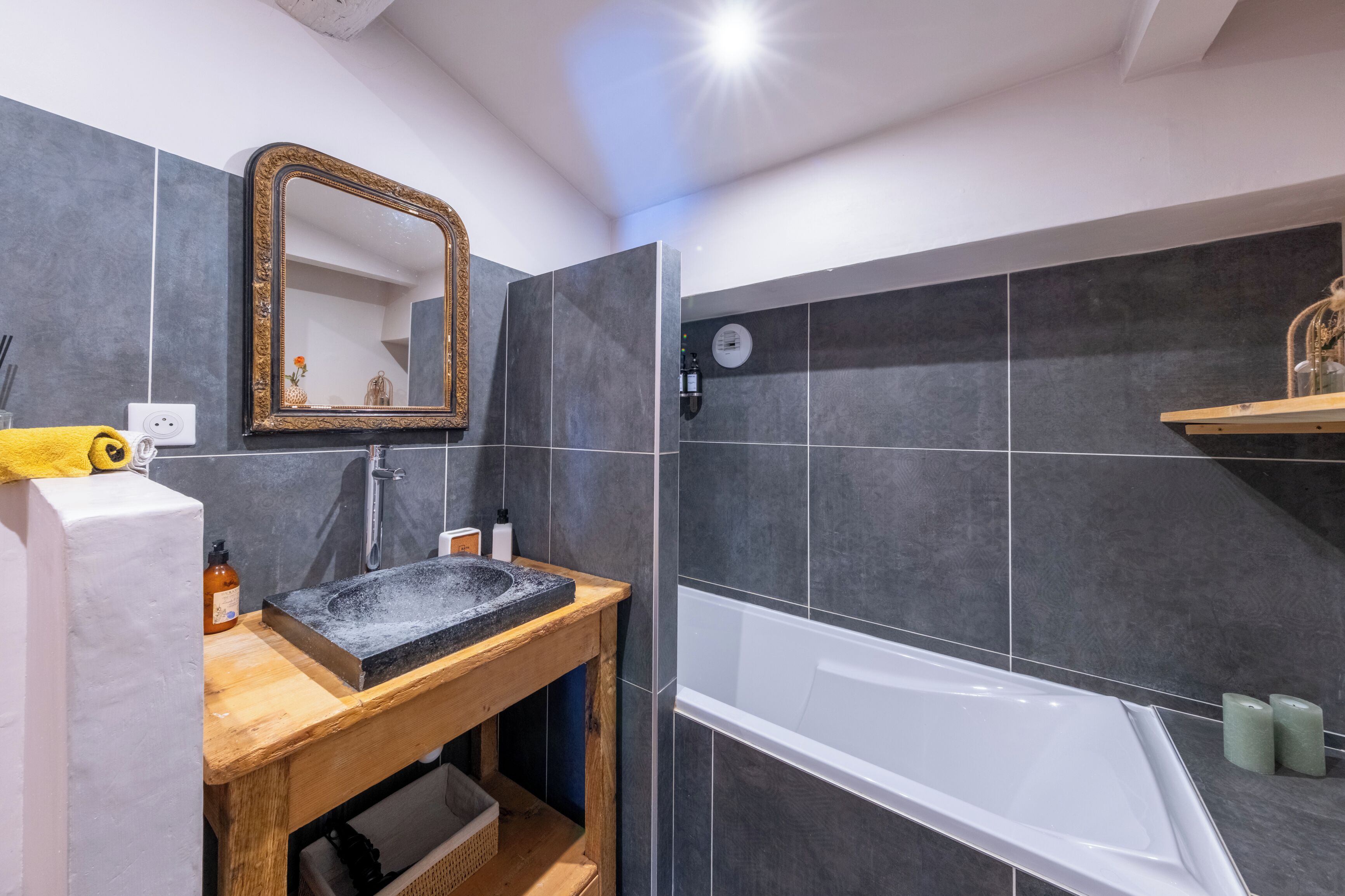 Un bagno con un mobile bagno in legno, un lavandino, uno specchio, una vasca e uno scaffale con articoli da toilette.