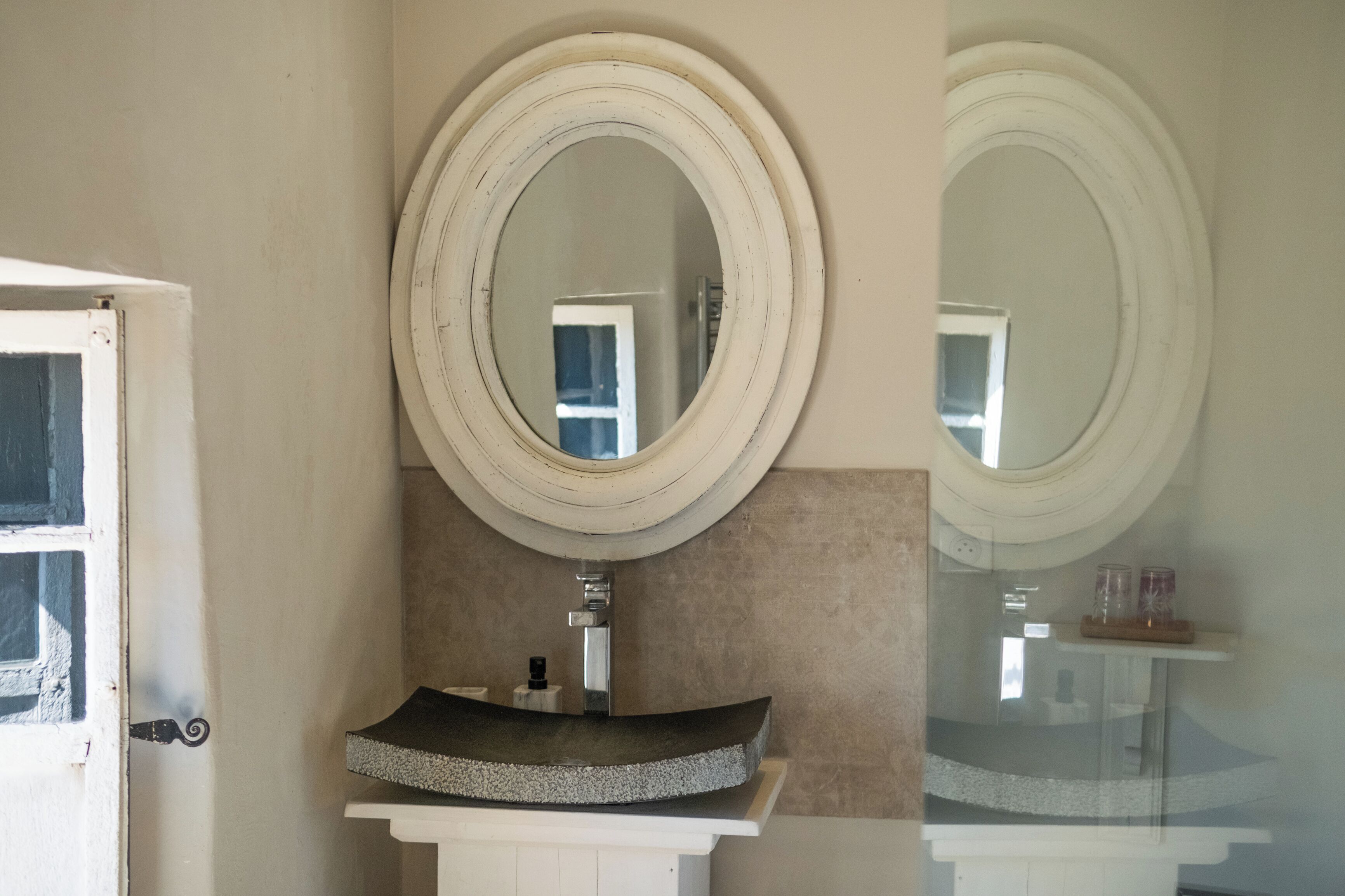 A bathroom with a round mirror, a sink, and a door.