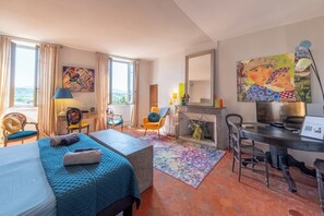 Una habitación de hotel con cama, escritorio, silla, chimenea y obras de arte en las paredes.