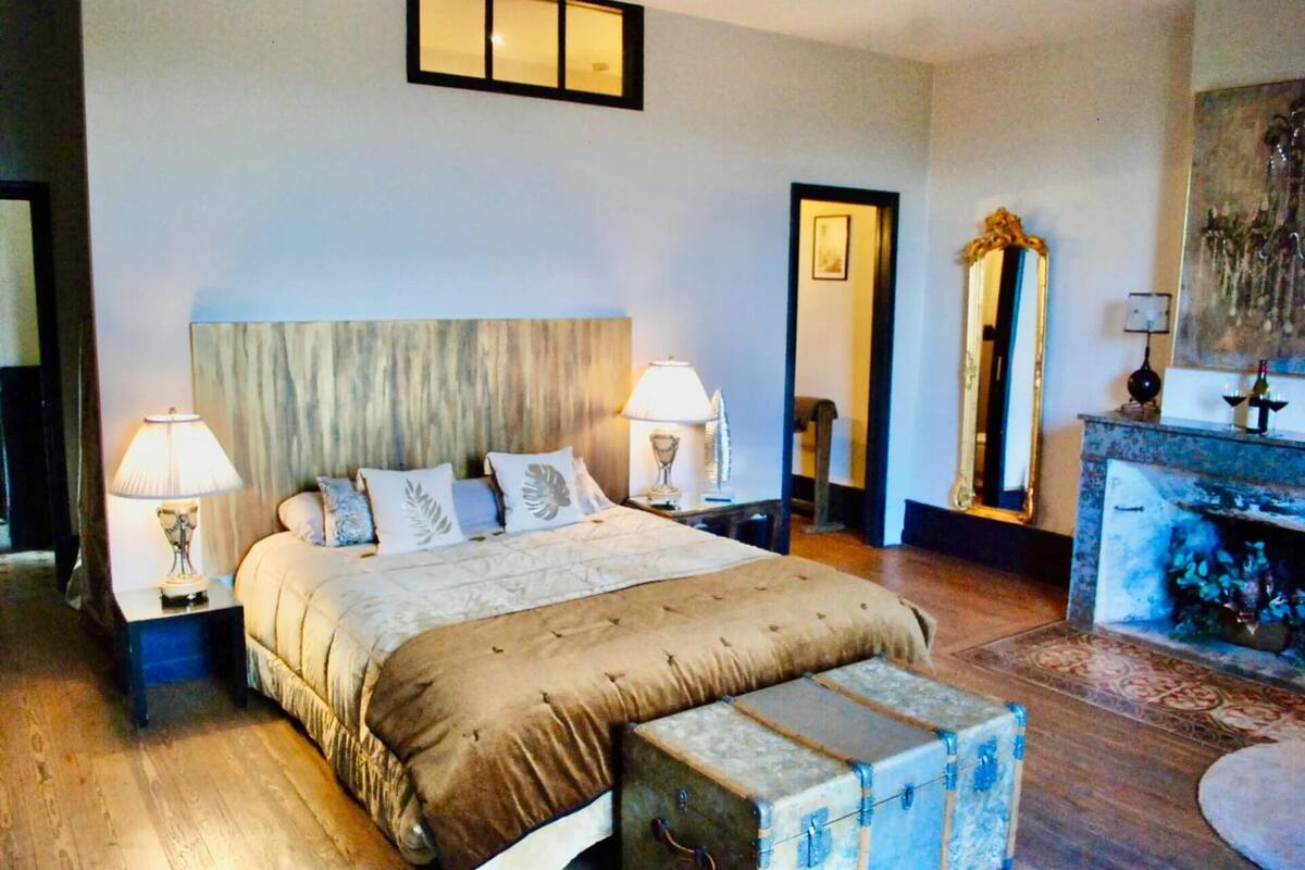 A bedroom with a large bed, bedside lamps, a dresser, a mirror, and a small table.