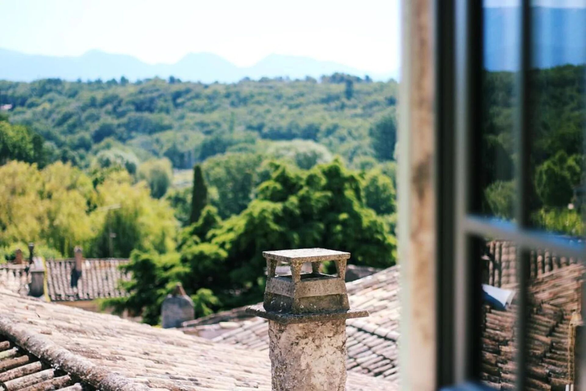 A view from a window overlooking a traditional tiled roof and a lush green landscape.