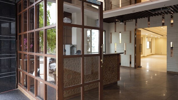 Una hall moderna di un hotel con una reception, un divisorio in vetro e vista sull'esterno.