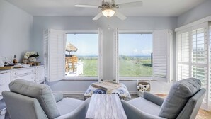 A room with a ceiling fan, two grey armchairs, a wooden coffee table, and a view of a grassy area through large windows. - Welcome to “Salty Dog” - named after the old sea captain, this beautiful house directly on the Atlantic Ocean is decorated throughout with a nautical theme. With the breathtaking view of the ocean out your back door you will feel as though you are ac (Indialantic)