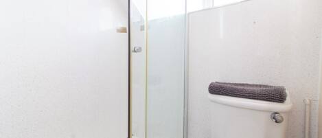 Un baño con cabina de ducha de vidrio, inodoro con toallero y pared blanca.