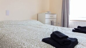 Un lit bien fait, recouvert d’une couvre-lit à motifs, une petite table de chevet avec une lampe et une fenêtre avec des rideaux.