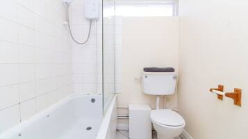 A small, clean bathroom with a white bathtub, toilet, and a glass shower enclosure.
