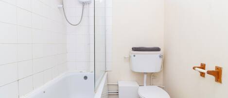 A small, clean bathroom with a white bathtub, toilet, and a glass shower enclosure.