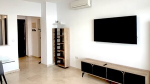 A modern living room with a flat-screen TV mounted on the wall, a wooden entertainment unit, and a built-in air conditioning unit. - Golden Sunrise – Santa Clara – direct access to the beach (Torremolinos)