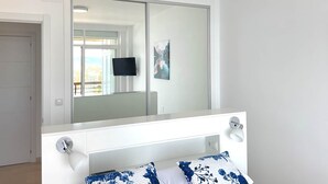 A bedroom with a large mirror, a television, and a bed with blue floral pillows. - Golden Sunrise – Santa Clara – direct access to the beach (Torremolinos)