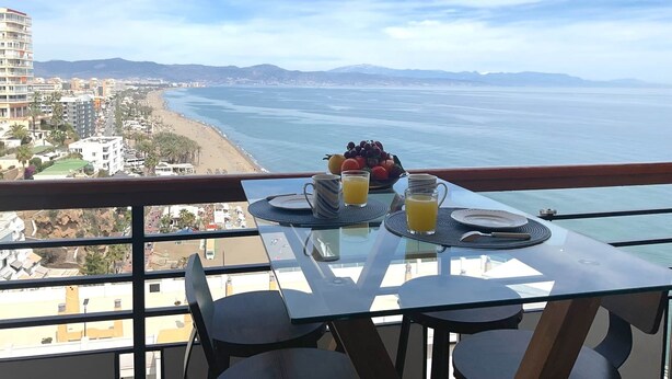 A balcony with a table set for breakfast, overlooking a beach and cityscape. - Golden Sunrise – Santa Clara – direct access to the beach (Torremolinos)