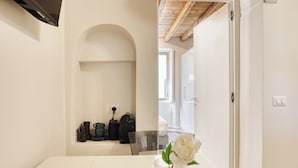A minimalist dining area with a white table, a clear glass vase with a white flower, and a black mug.