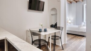 A modern room with a white table, two chairs, a TV mounted on the wall, and a bed with a wooden ceiling.