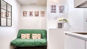 A compact living space with a green sofa, a white kitchenette, and a small dining area.