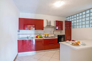 Une cuisine moderne avec des meubles de rangement rouges, une cuisinière à gaz et un coin repas où l’on peut prendre le petit-déjeuner avec des croissants et des fruits.